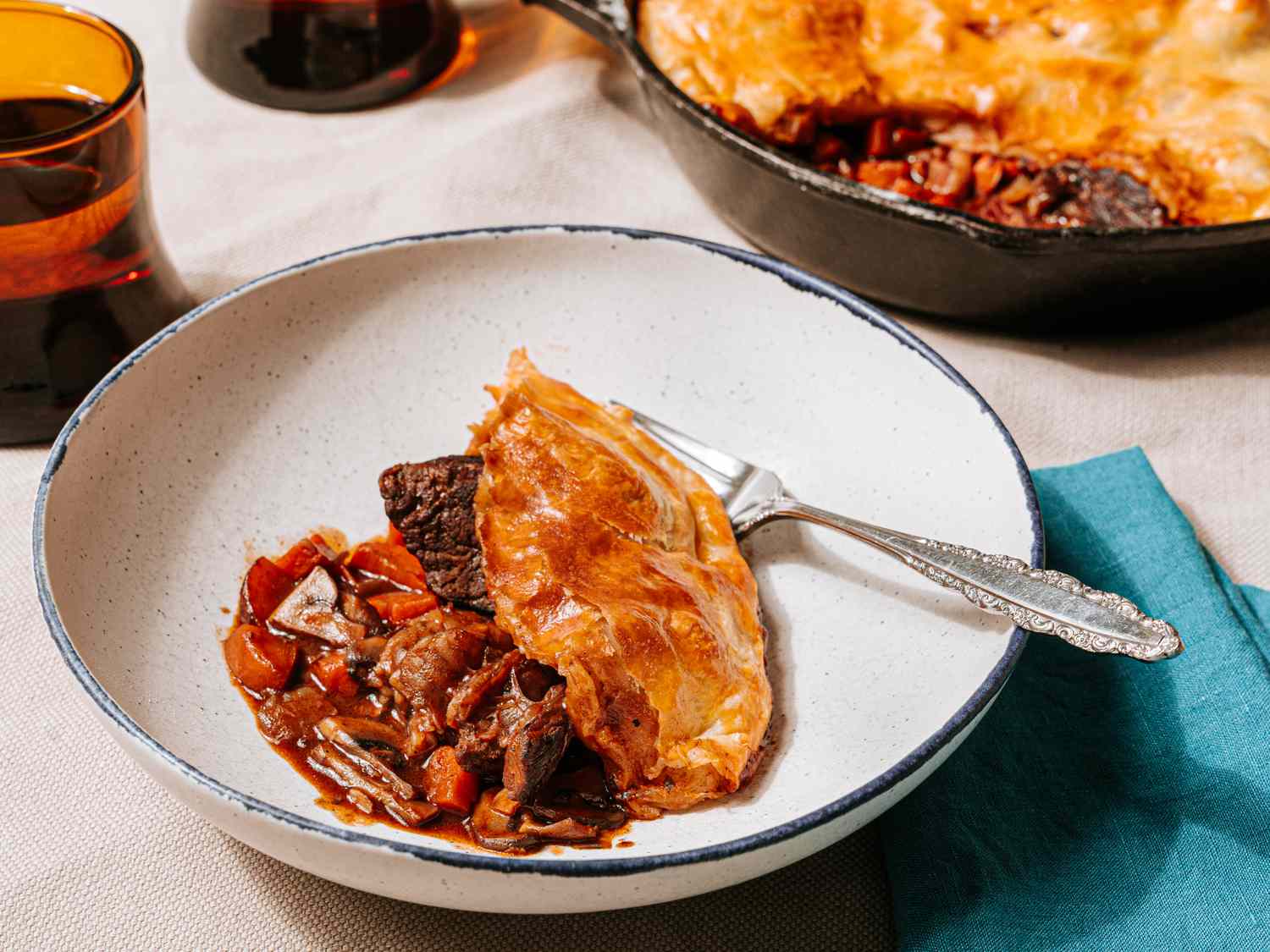 Beef bourguignon pot pie served in a bowl with a fork garnished and plated from a larger pot pie dish in view