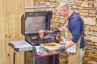 A person using tongs to move steaks from the Weber Spirit E-310 Gas Grill onto a tray