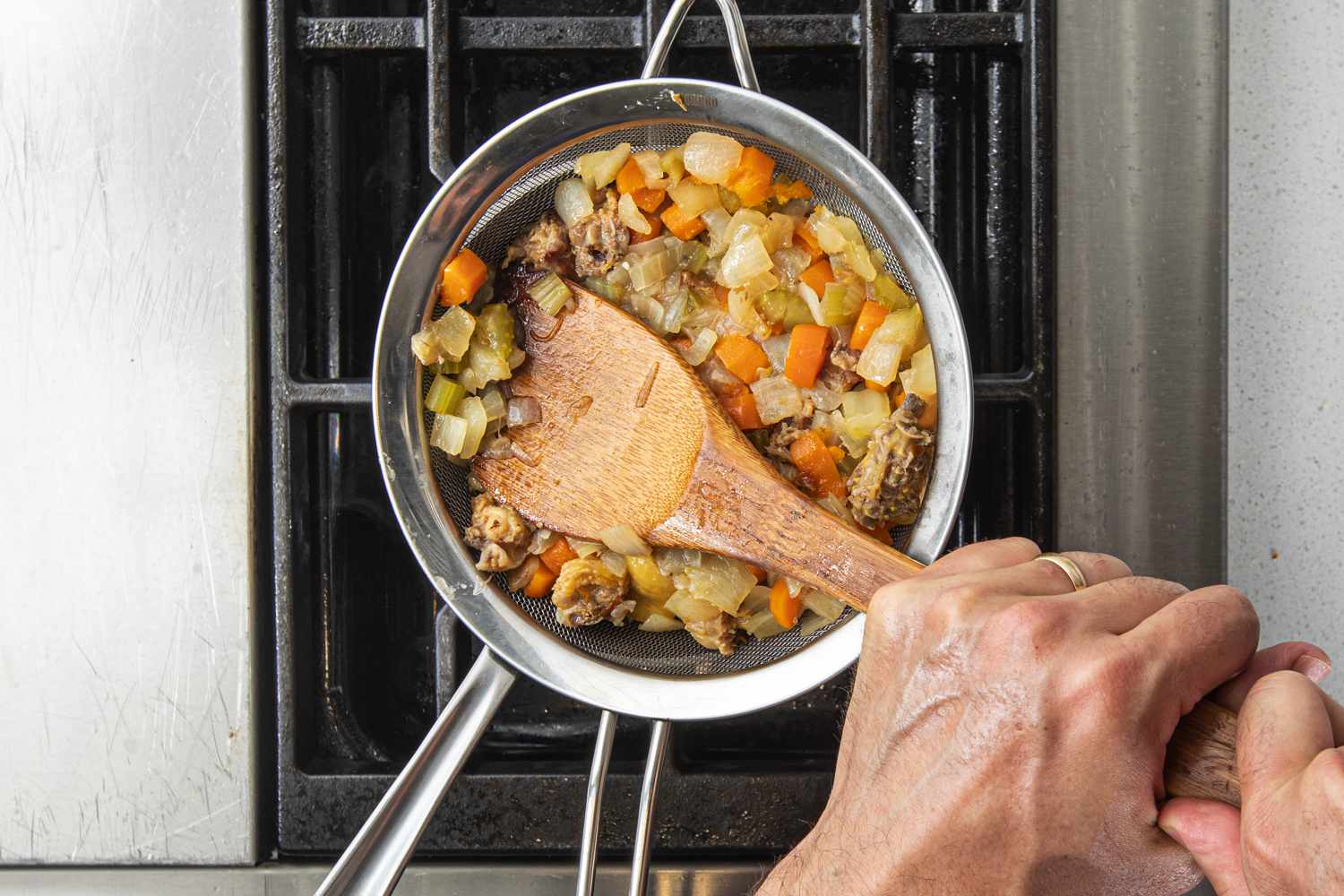 Overhead view straining vegetables and chicken back pieces out of a simmered jus mixture.