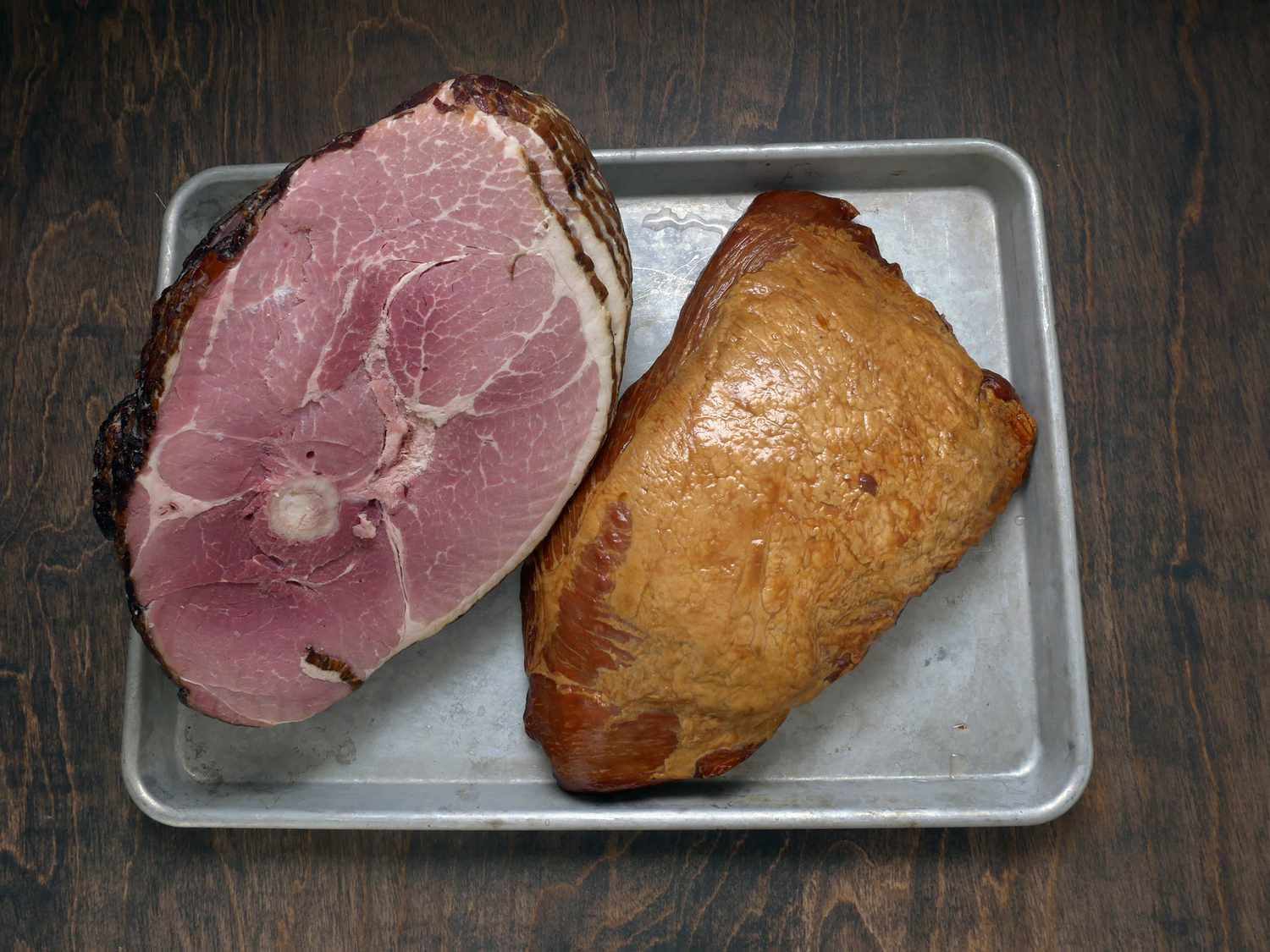 a bone-in ham next to a boneless ham on a sheet tray