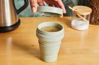 A person removing the lid of a Stojo travel cup filled with coffee.