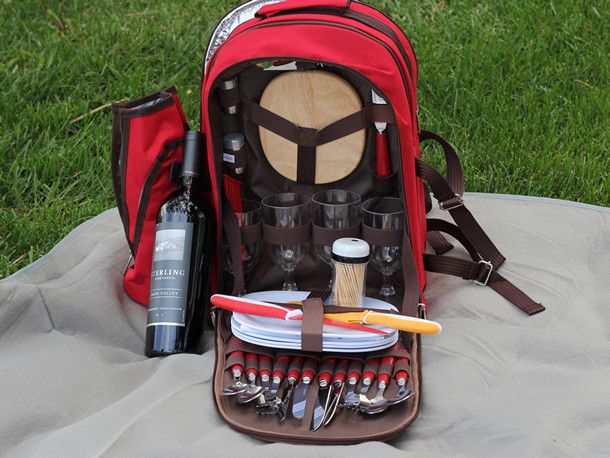 The inside of a red picnic backpack shows toothpicks, plates, glasses, and utensils inside, along with a bottle of wine. 
