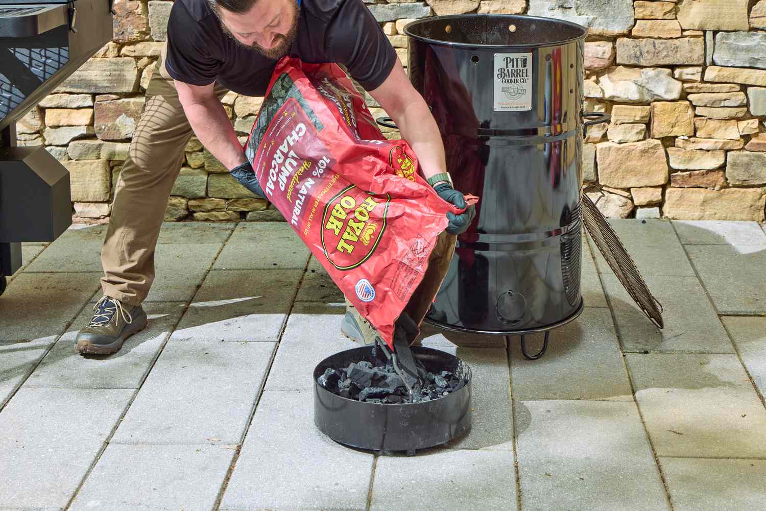 A person pours charcoal into the Pit Barrel Cooker Co. Classic Pit Barrel Cooker