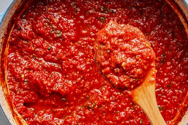 A pot of tomato sauce with a wooden spoon lifting some sauce