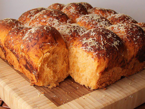 Closeup of pizza bread being cut into rolls on a bamboo cutting board.