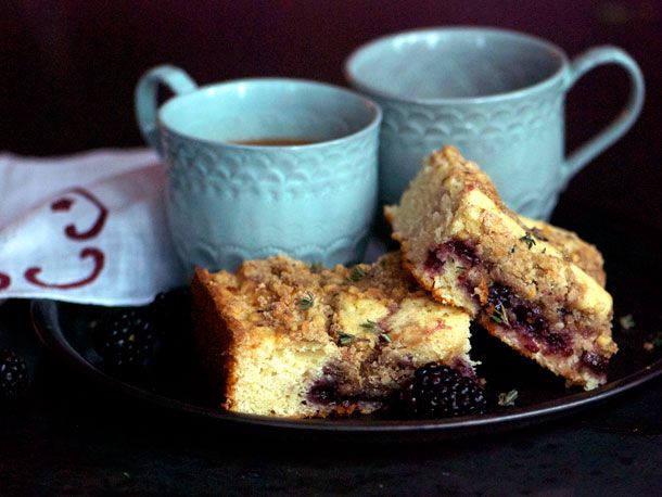 Two slices of blackberry thyme crumb cake, served on a black plate with two mugs of coffee.