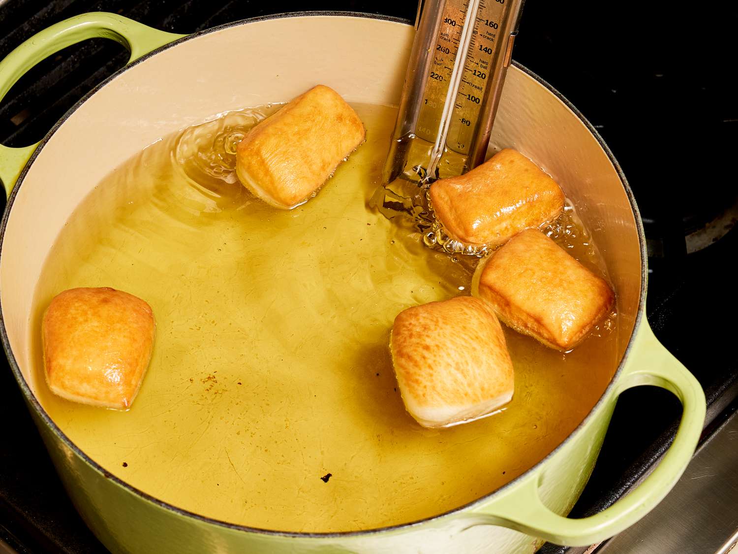 Beignets cooking in oil, flipped so browned side is visible 