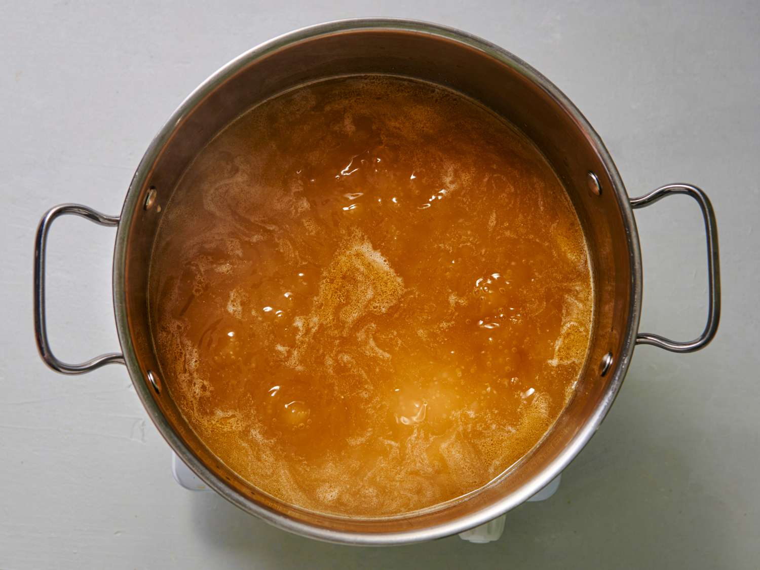 A large stainless steel pot holding the broth mixed with the cornstarch mixture, soy sauce, and sesame oil. The contents are at a boil.