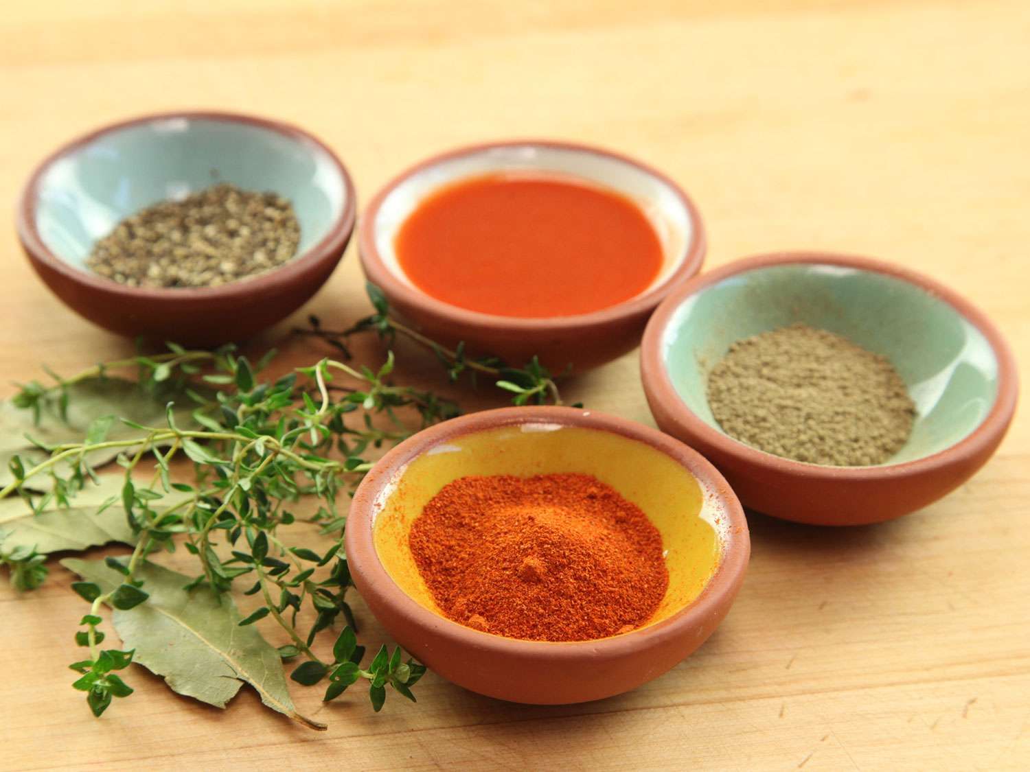 Pinch bowls holding various seasonings for red beans and rice, plus dried bay leaves and fresh thyme sprigs.