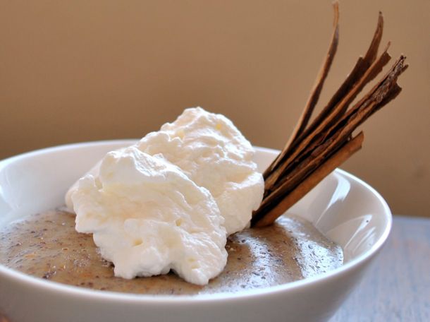 Closeup of cinnamon-orange pudding, served in a small white bowl with a slivered canela cinnamon garnish and whipped cream.