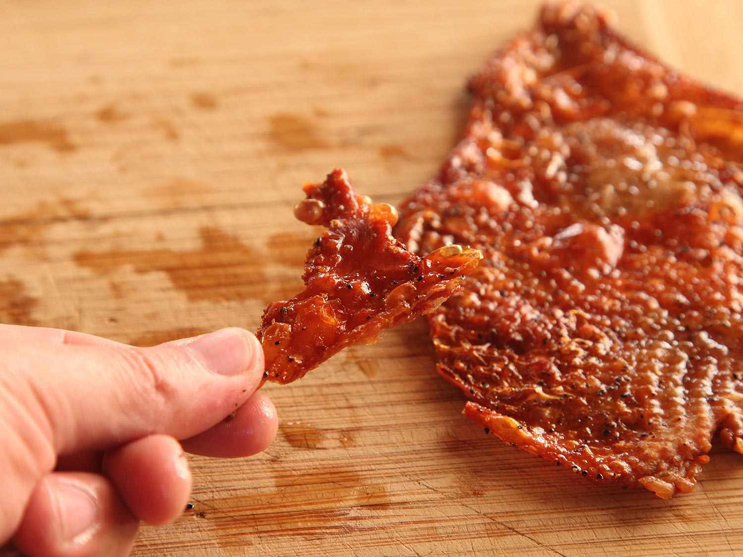Fingers holding crisp roasted turkey skin broken into a bite-sized shard.