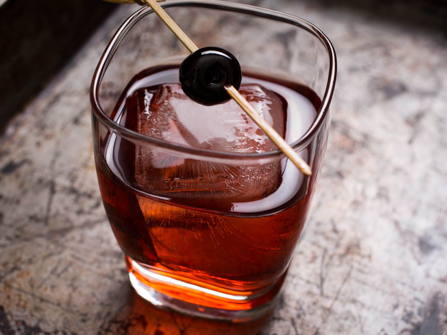 A boulevardier cocktail served with a large ice cube and a Luxardo cherry garnish.