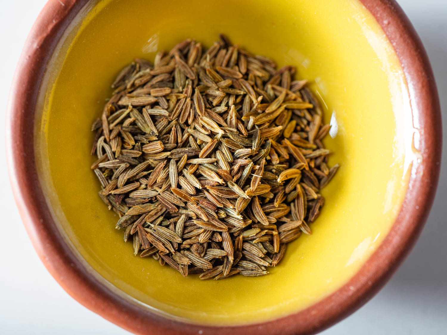 Close-up overhead shot of a yellow ceramic bowl of whole cumin seeds