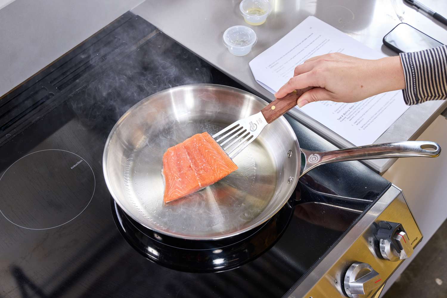 A person flips a piece of salmon in the Le Creuset 12 Inch Large Tri-Ply Stainless Steel Fry Pan