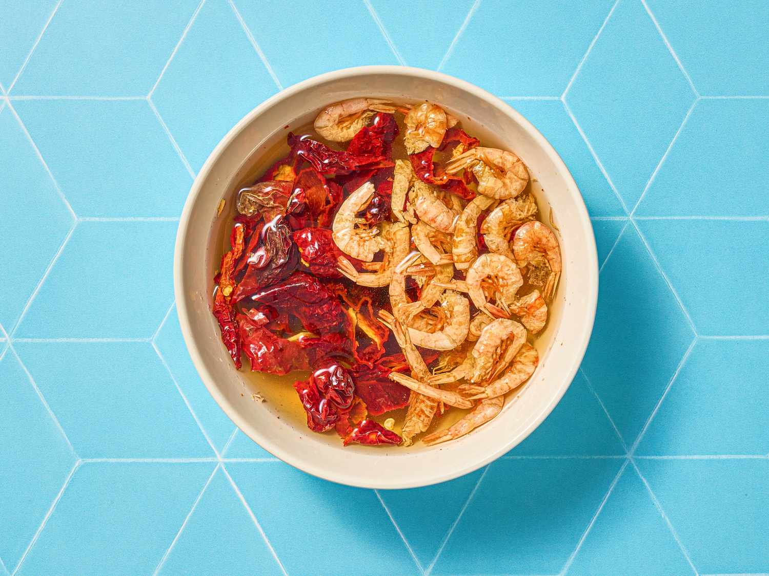A bowl of curry laksa with shrimp and red chili served on a blue geometricpatterned background
