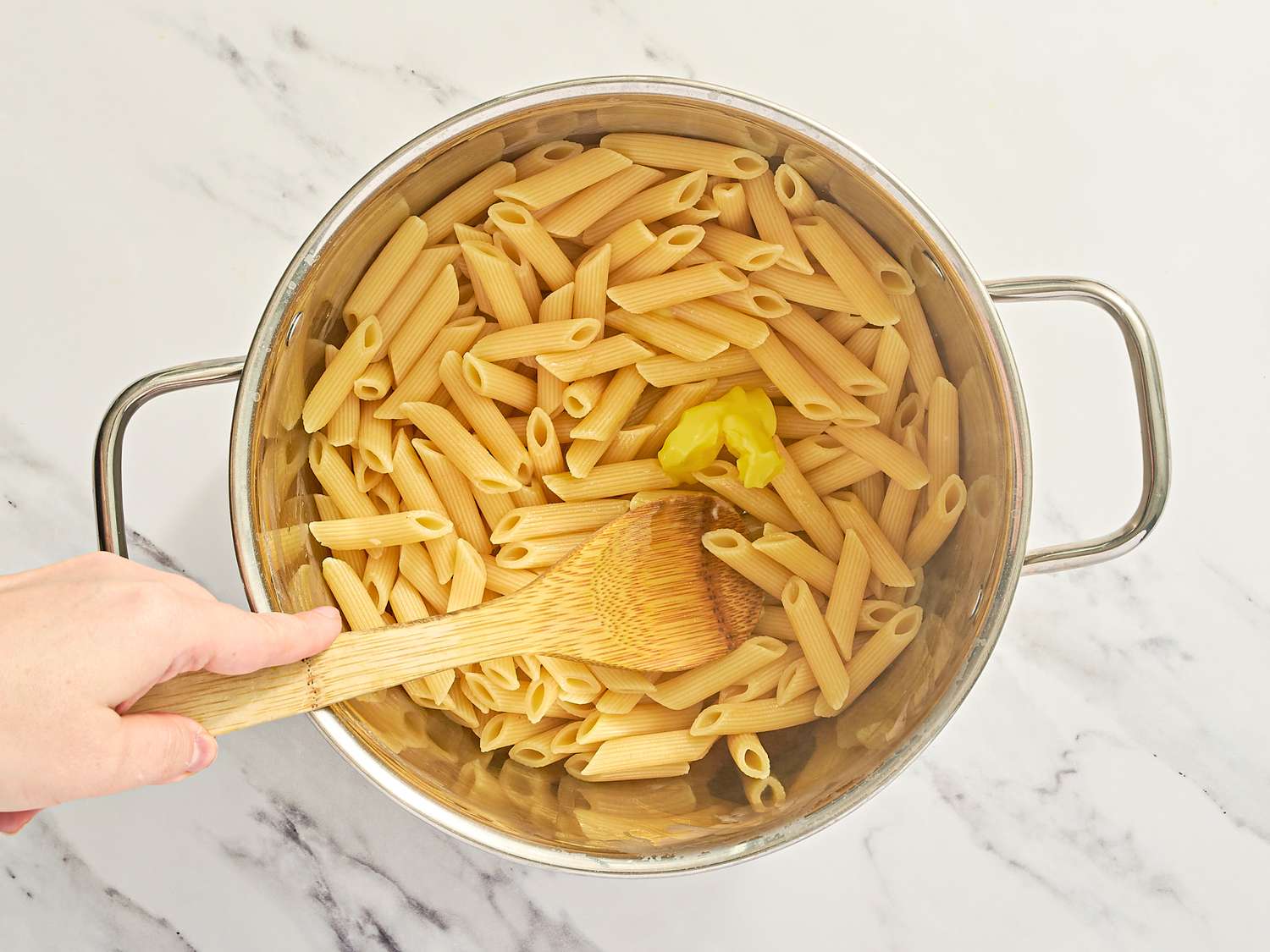 Cooking pasta in a pot with a piece of butter and a wooden spoon