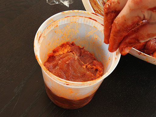 A hand layering marinated pork in quart-sized deli container
