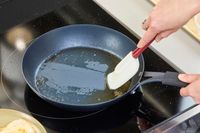 A person scrapes the bottom of the OXO Obsidian 10 Inch Pre-Seasoned Carbon Steel Frying Pan
