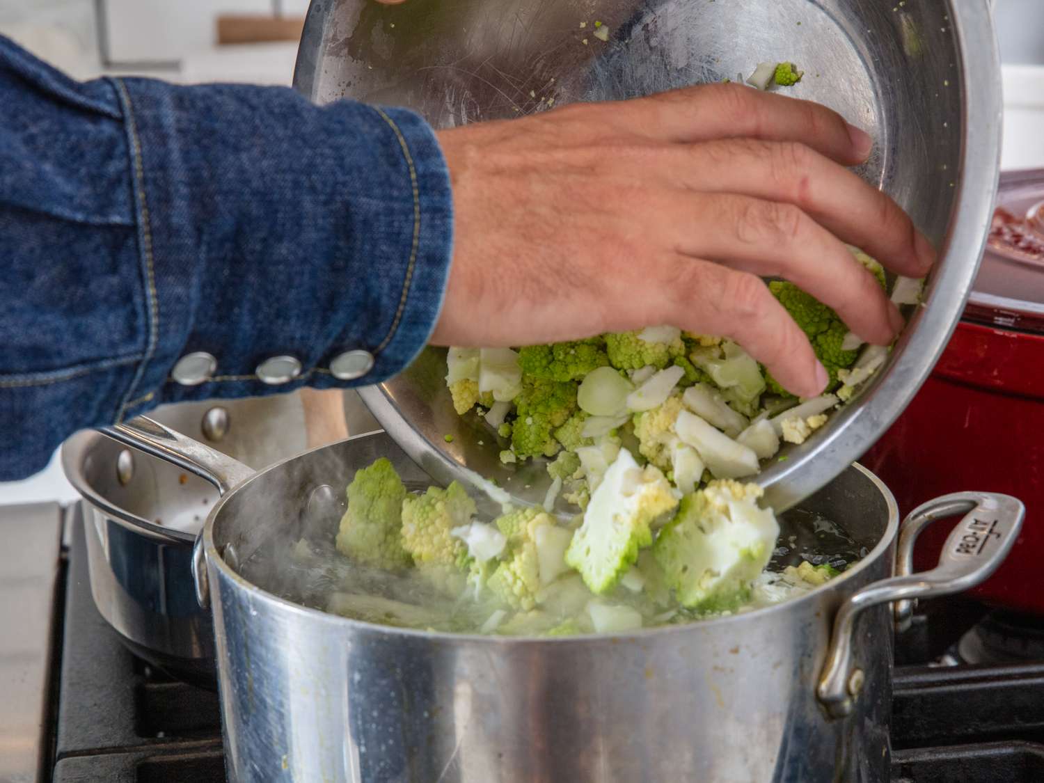 A person adding chopped romanesco to a pot on a stove