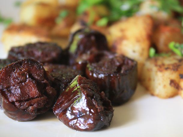 Pieces of morcilla served with potatoes on a white plate. 