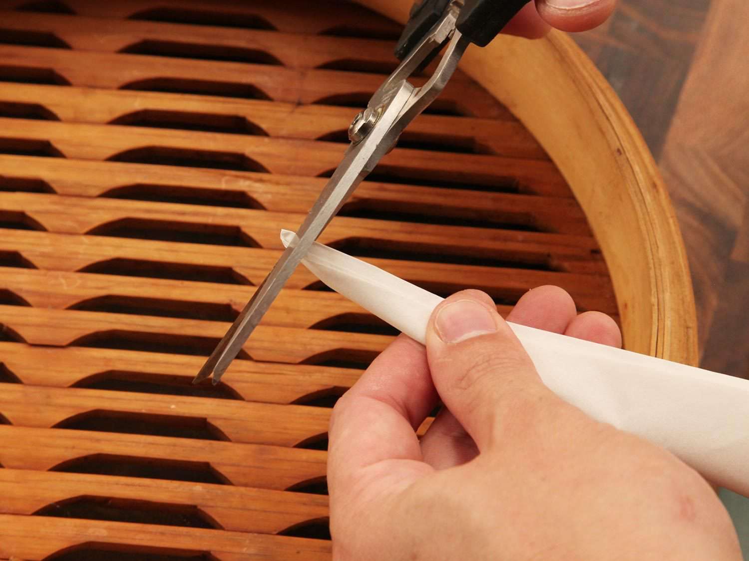Cutting the tip off a parchment paper triangle to get the right size to line a bamboo steamer basket.