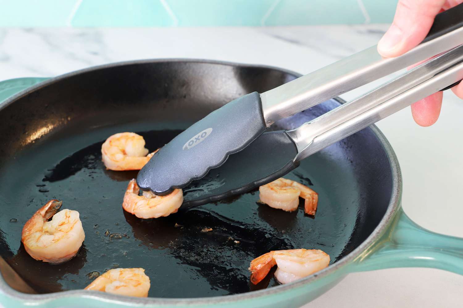 Hand using the OXO 12-Inch Silicone Tongs to pick up shrimp