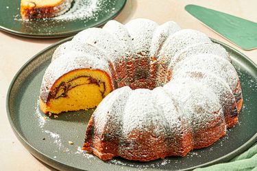 A bundt cake with a slice removed revealing a swirled interior design dusted with powdered sugar placed on a plate