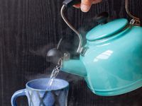 a person pouring water from a blue kettle into a mug