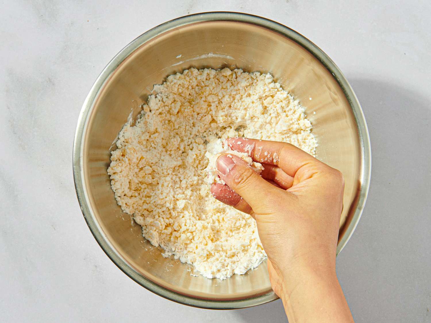 Hand mixing ingredients in a bowl containing crumbled mixture a step in a cooking preparation process