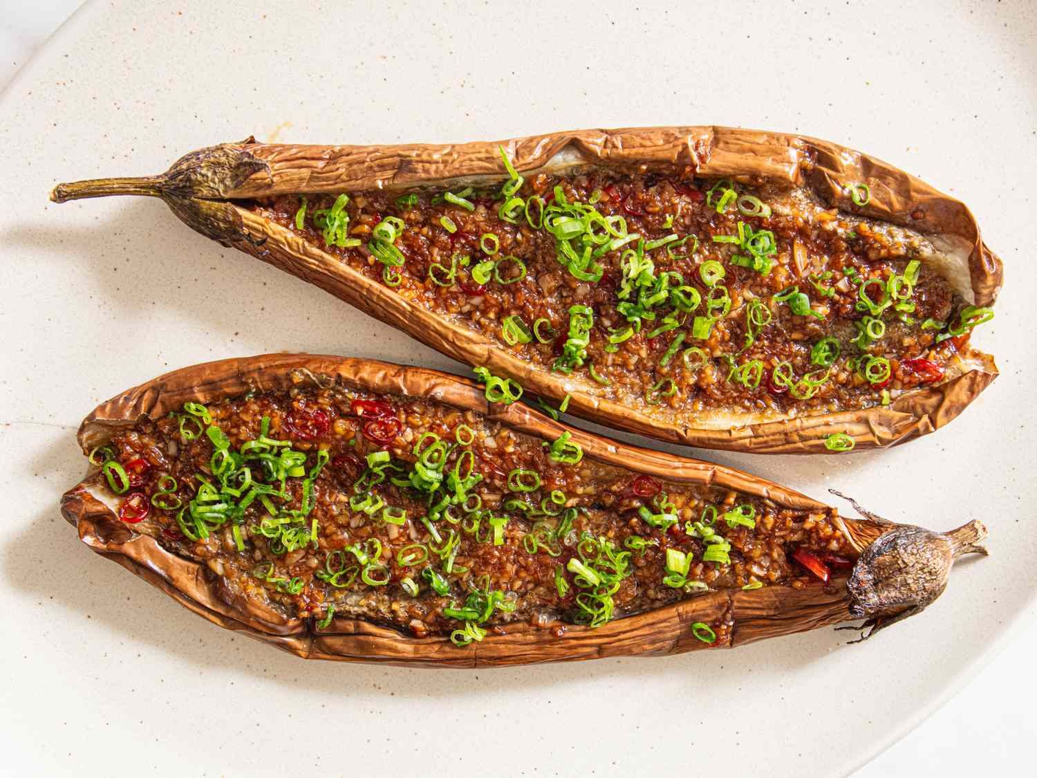 Two roasted Chinese barbecue eggplants topped with green onions served on a white plate