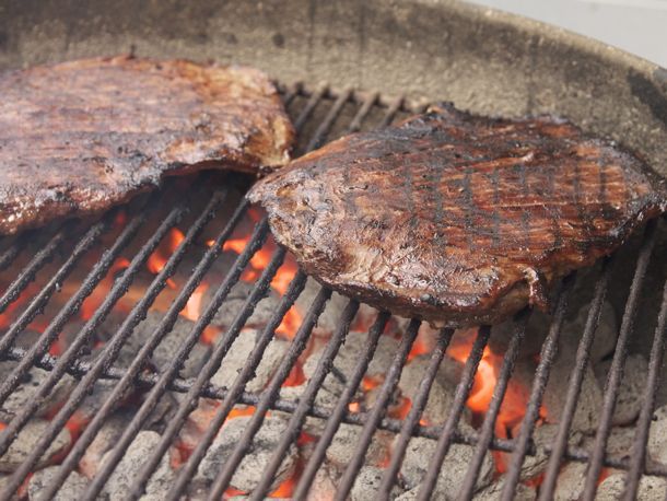 Two pieces of flank steaks charring on the grill. 