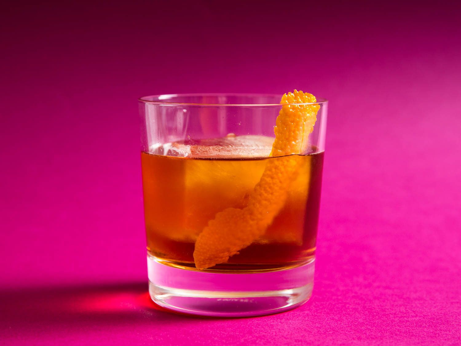 Tequila Negroni Cocktail over ice in rocks glass against magenta background