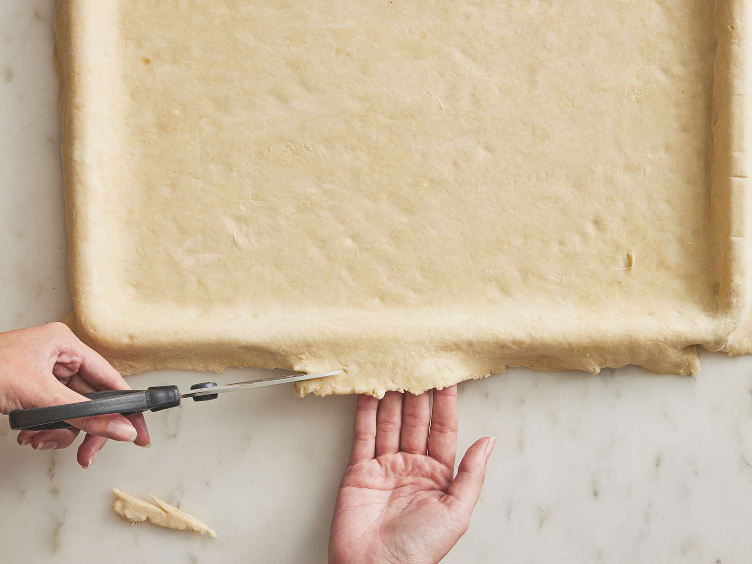 Cutting the edges of dough that has been spread onto a pan 
