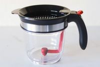 A transparent container with a black lid handle and a red lever mechanism inside