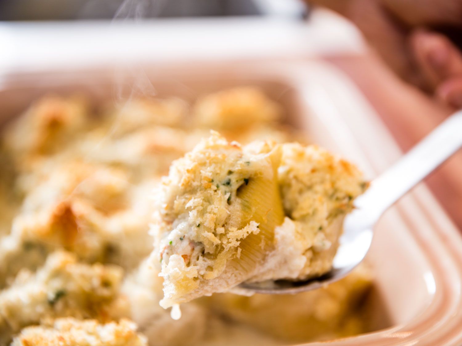 Holding up a spoon of baked seafood stuffed pasta shells. 