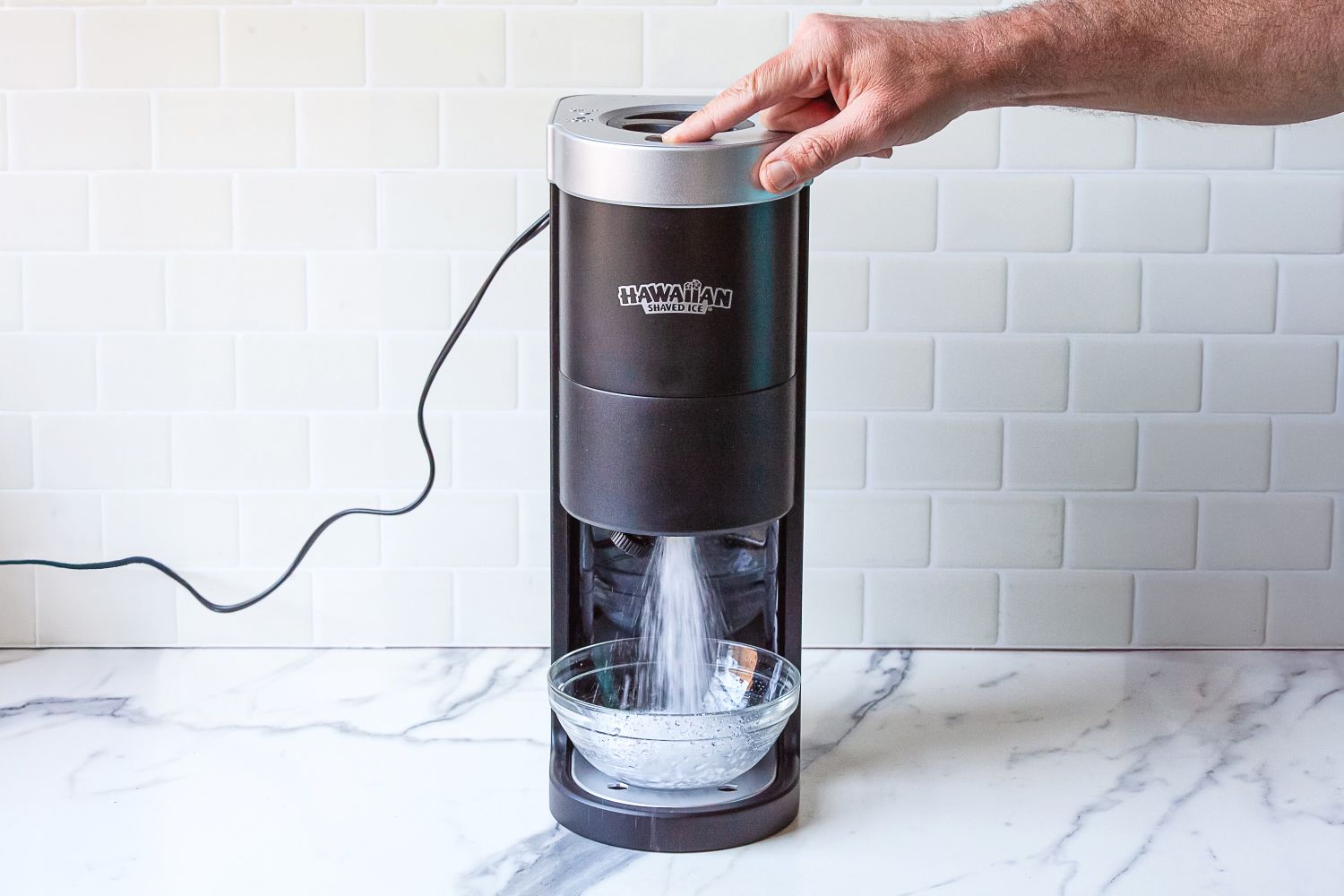 A person operating Hawaiian Shaved Ice HomePro Shave Ice and Snow Cone Machine (S777) with ice falling into a bowl
