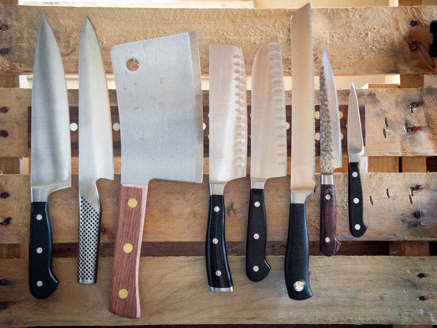 An assortment of knives on a magnetic strip, attached to a wooden pallet