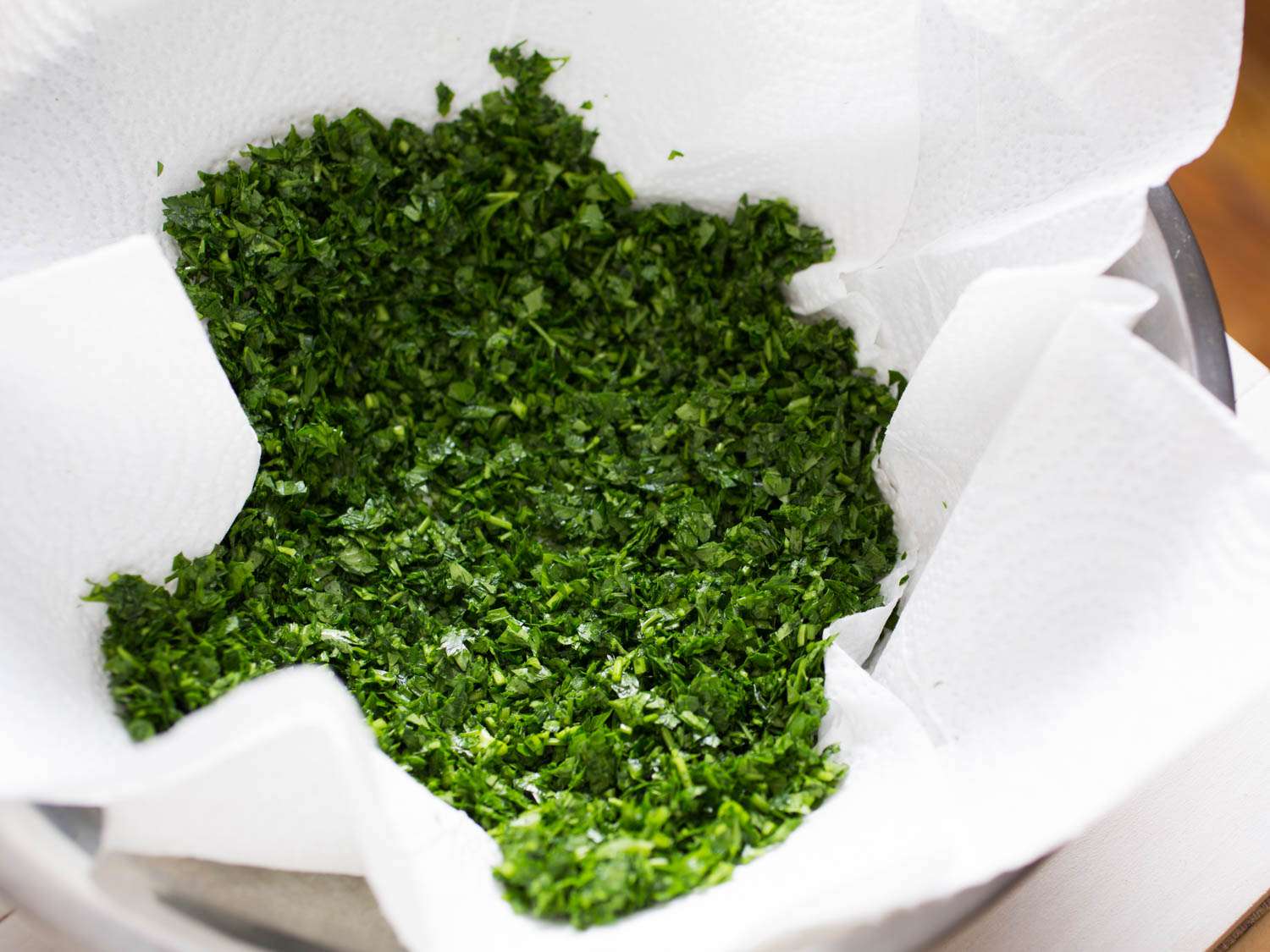 Finely chopped parsley for tabbouleh in a mixing bowl lined with paper towel.