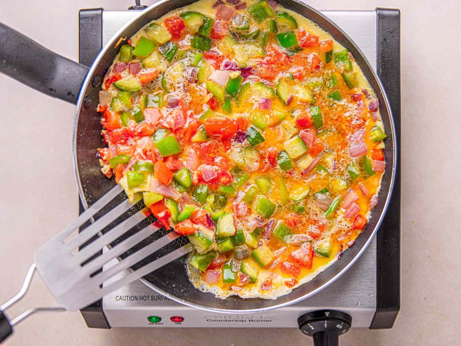 Omelet cooking in a pan on a stovetop with vegetables being sauted