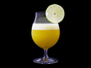 Frothy fresh pineapple margarita in footed cocktail glass against black background