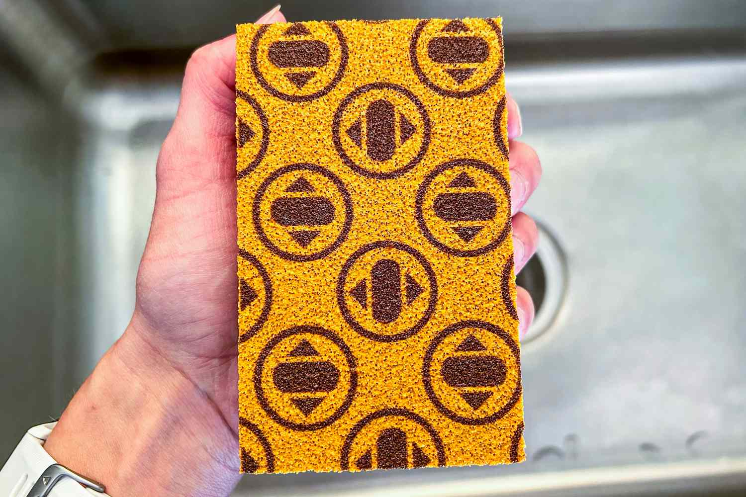 An orange Skura dishwashing sponge being held over a kitchen sink