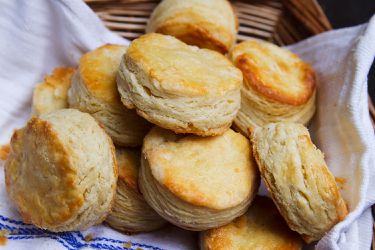 A towel-lined basket full of buttermilk biscuits. 