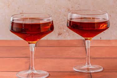 Two Manhattans in stemmed cocktail glasses on a wooden surface