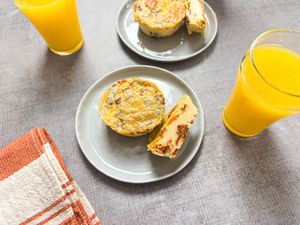 Two plates with muffin tin bacon egg bites next to glasses of orange juice