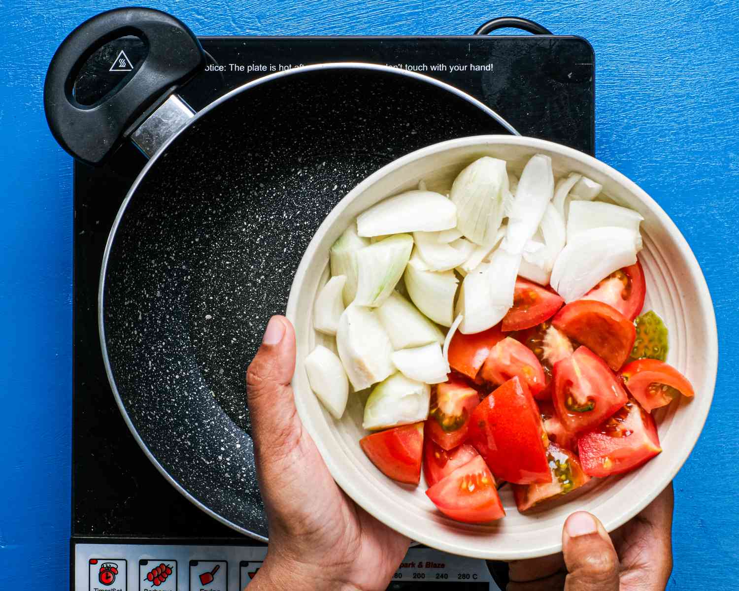 Overhead view of onions and tomatoes being added to pan