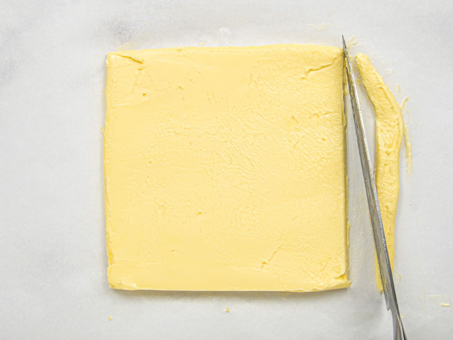 A square piece of butter with a knife trimming one edge