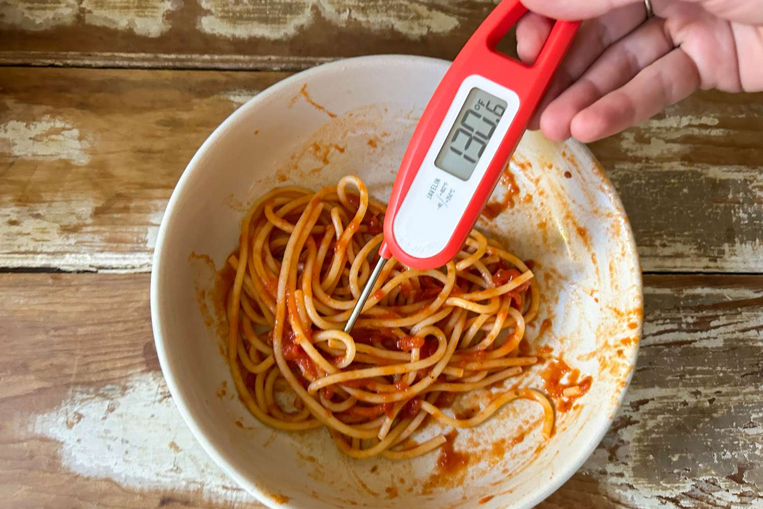 An instant-read thermometer is inserted into a saucy bowl of spaghetti.