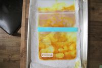 Sealed bags on a tray containing food marinated with a yellow substance, laid on paper towels