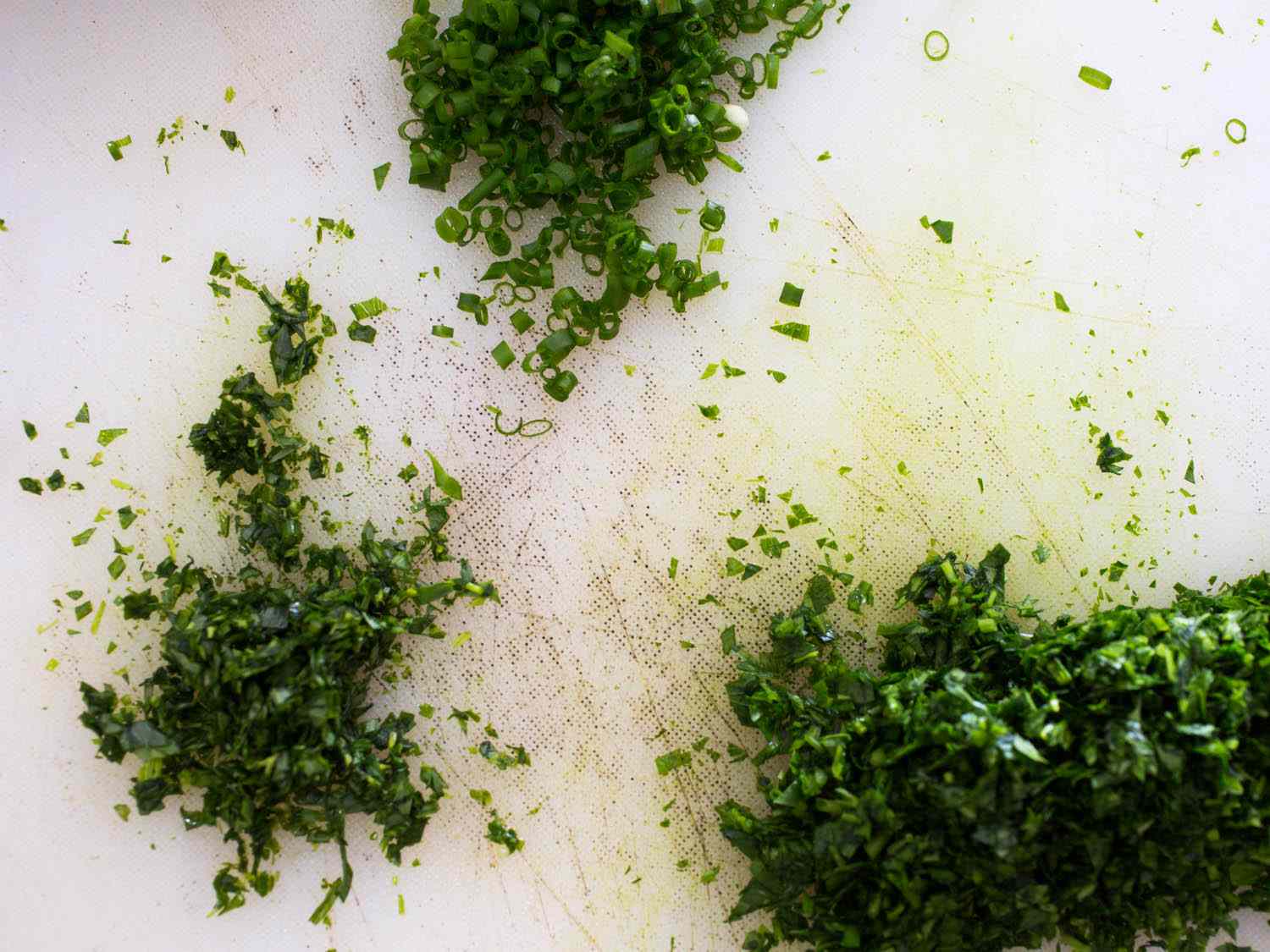 Finely chopped green fresh herbs, resting on a white cutting board.