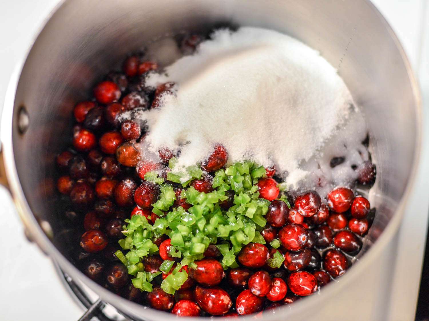 Ingredients for cranberry sauce in a saucepan: cranberries, sugar, lime juice and lime zest, and water. 